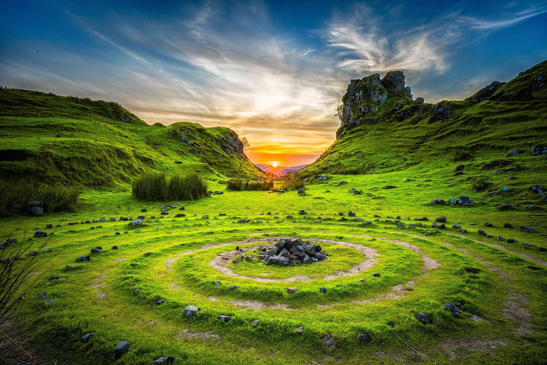 A spiral of stones in a green valley at sunrise